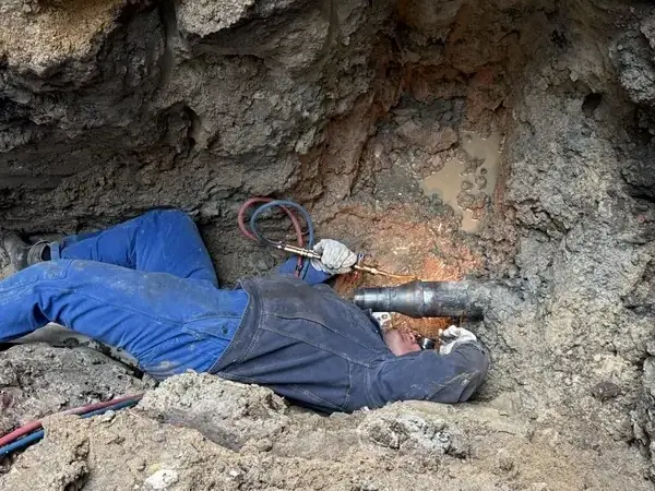 Hydraulik naprawia awarię rury wodnej w wykopie